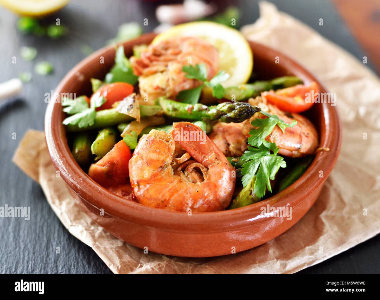 Delicious shrimp or seafood meal with green asparagus, tomatoes and decorative parsley. Spanish tapas plate in a bowl, close-up shot. Gourmet food. Stock Photo