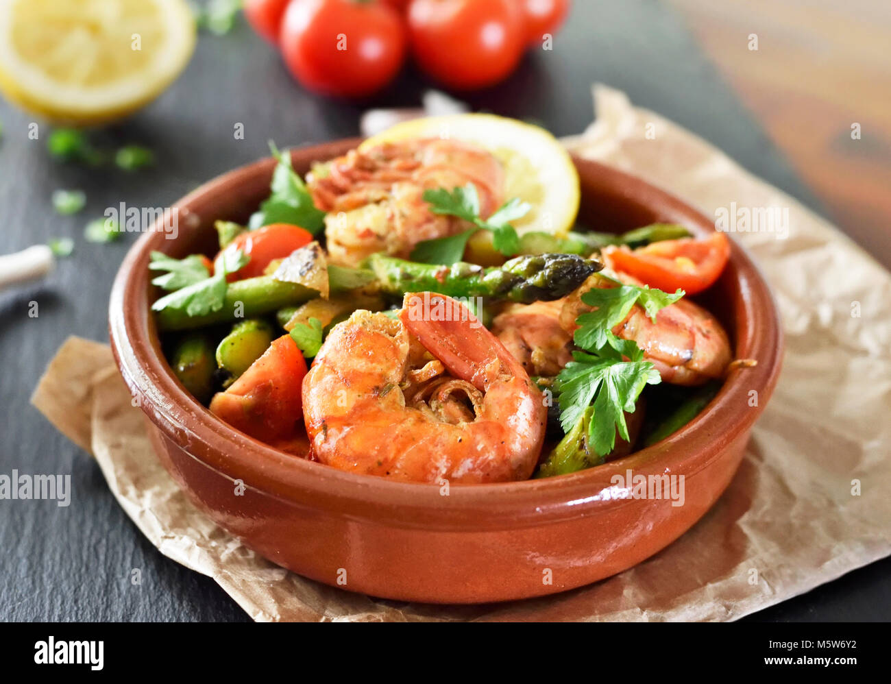 Delicious shrimp or seafood meal with green asparagus, tomatoes and decorative parsley. Spanish tapas plate in a bowl, close-up shot. Gourmet food. Stock Photo