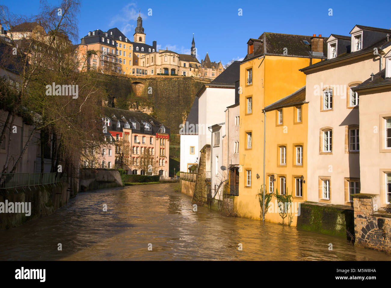 a view of the Alzette River as it passes through the Grund Quarter in Luxembourg City, Luxembourg, and the Ville Haute Quarter on the top left, highli Stock Photo