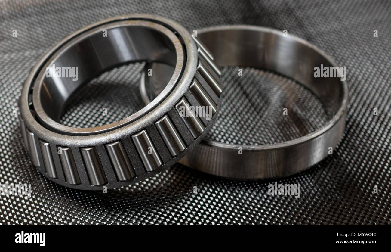 Antique automotive tapered roller bearing and race on plain weave carbon fiber cloth. Stock Photo
