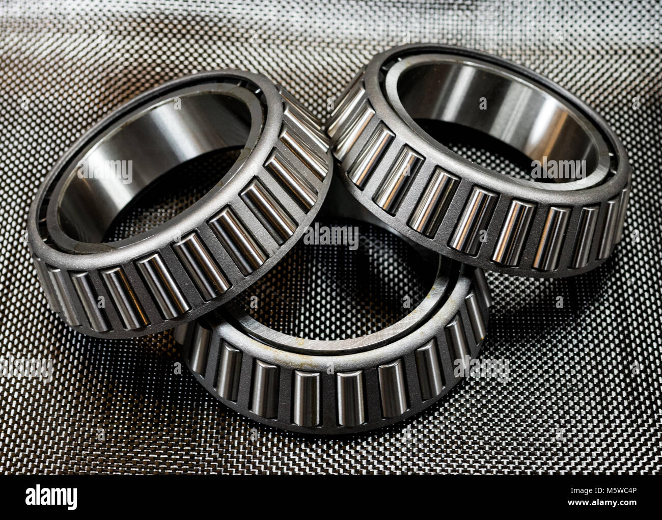 3 antique automotive tapered roller bearings on plain weave carbon fiber. Stock Photo