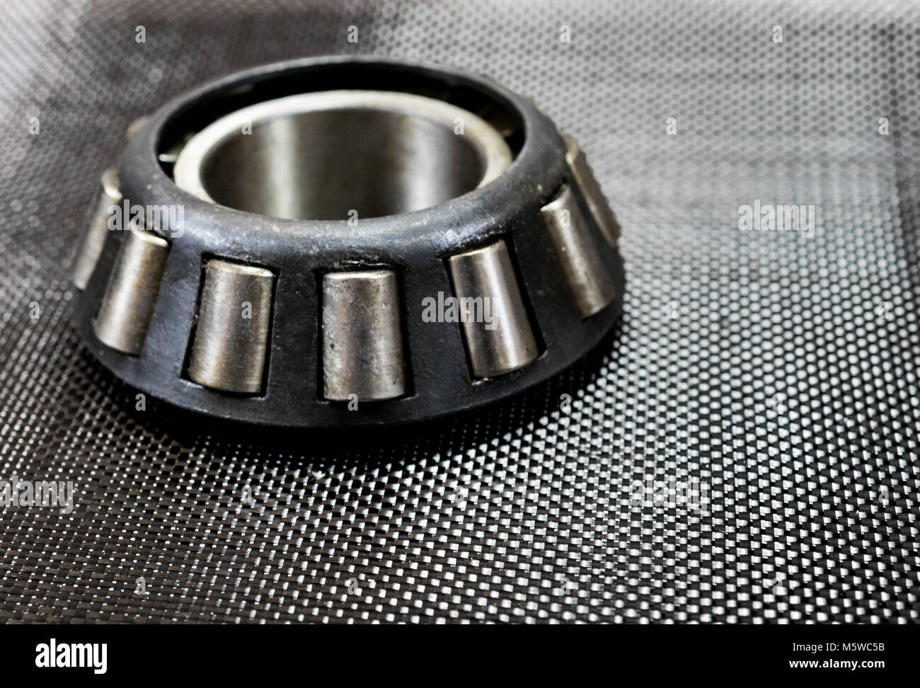 Antique automotive tapered roller bearing on plain weave carbon fiber. Stock Photo