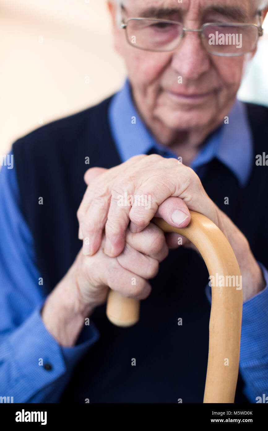 Sad Senior Man Sitting In Chair Holding Walking Cane Stock Photo