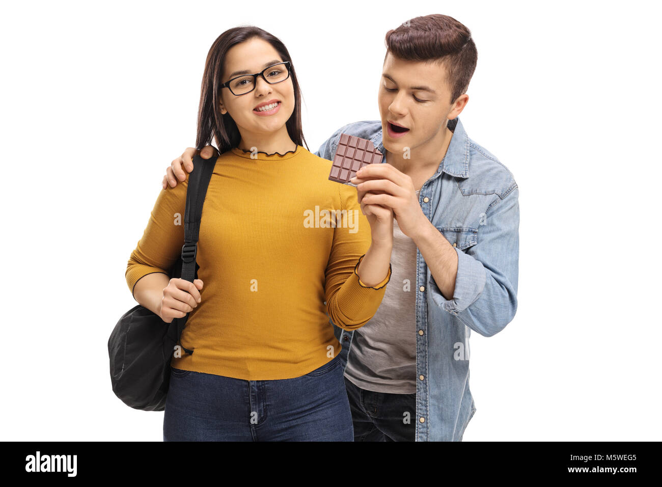 Teenage boy sneaking up on a female student to grab a bite of her chocolate isolated on white background Stock Photo
