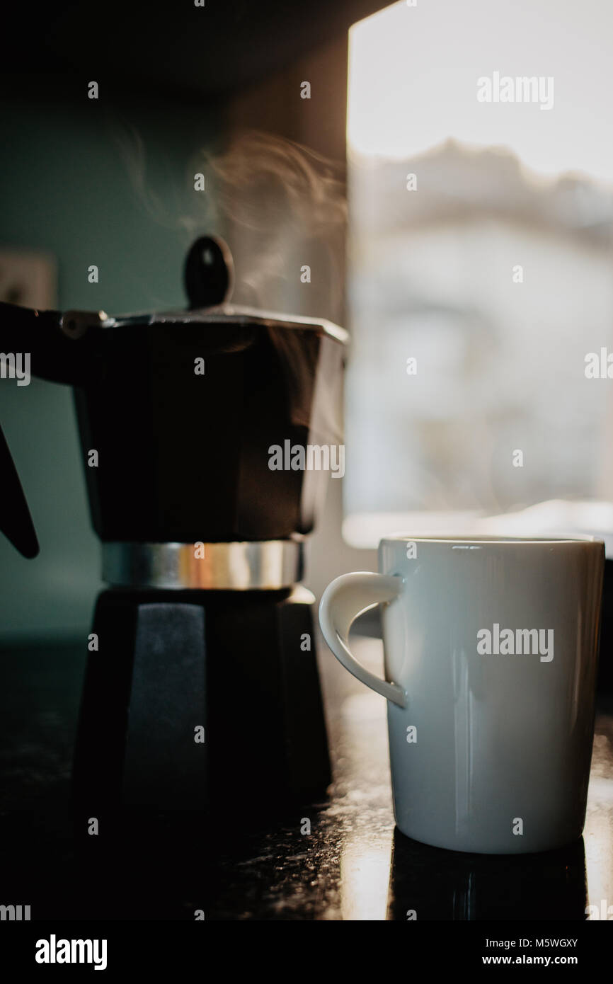 Preparing fresh coffee in moka pot on electric stove. A white mug of