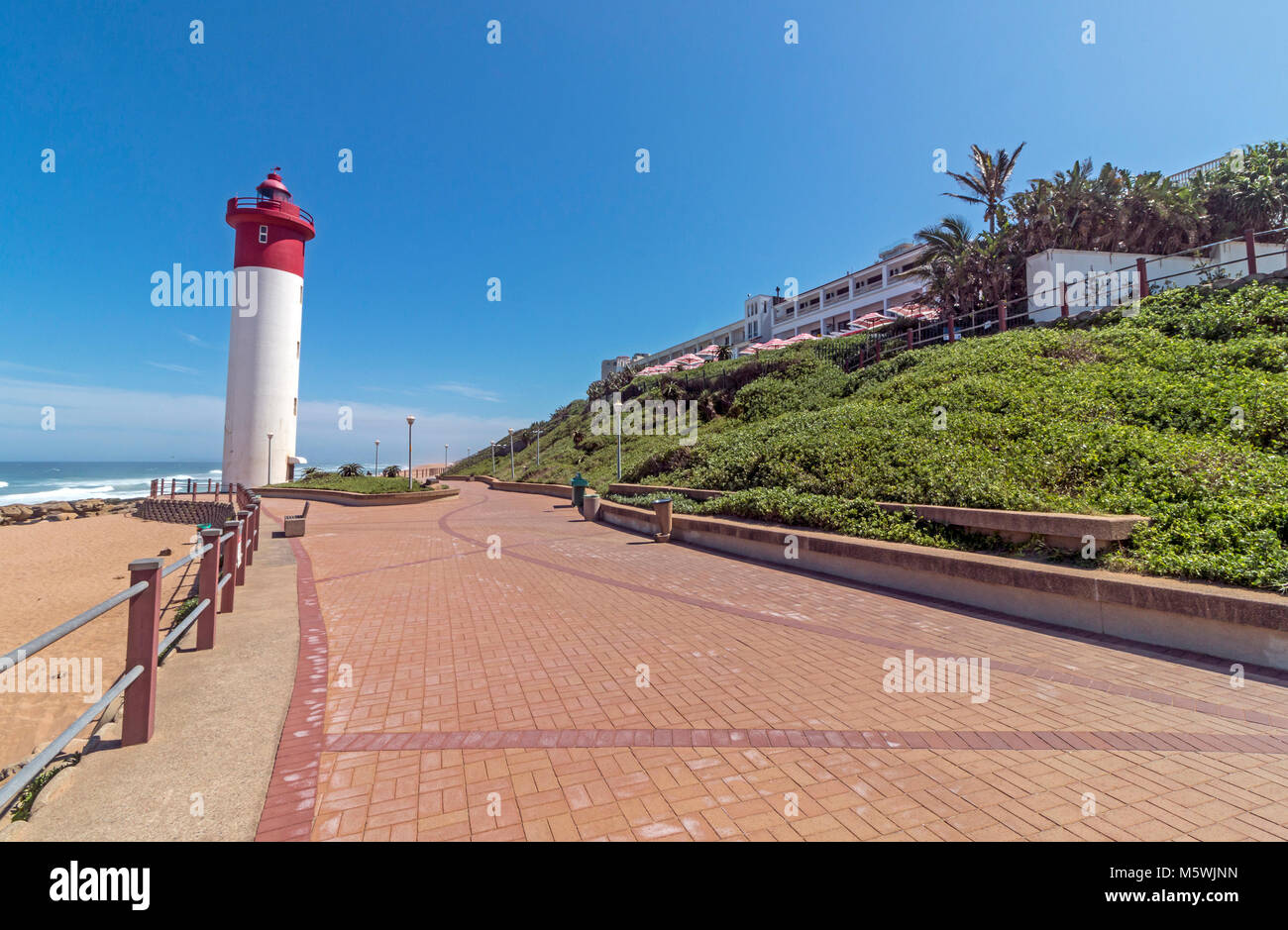 red-and-white-lighthouse-on-paved-beachfront-promenade-against-blue-sky