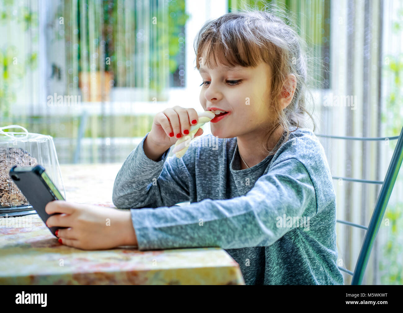 Little girl eating candy and looking at mobile phone Stock Photo