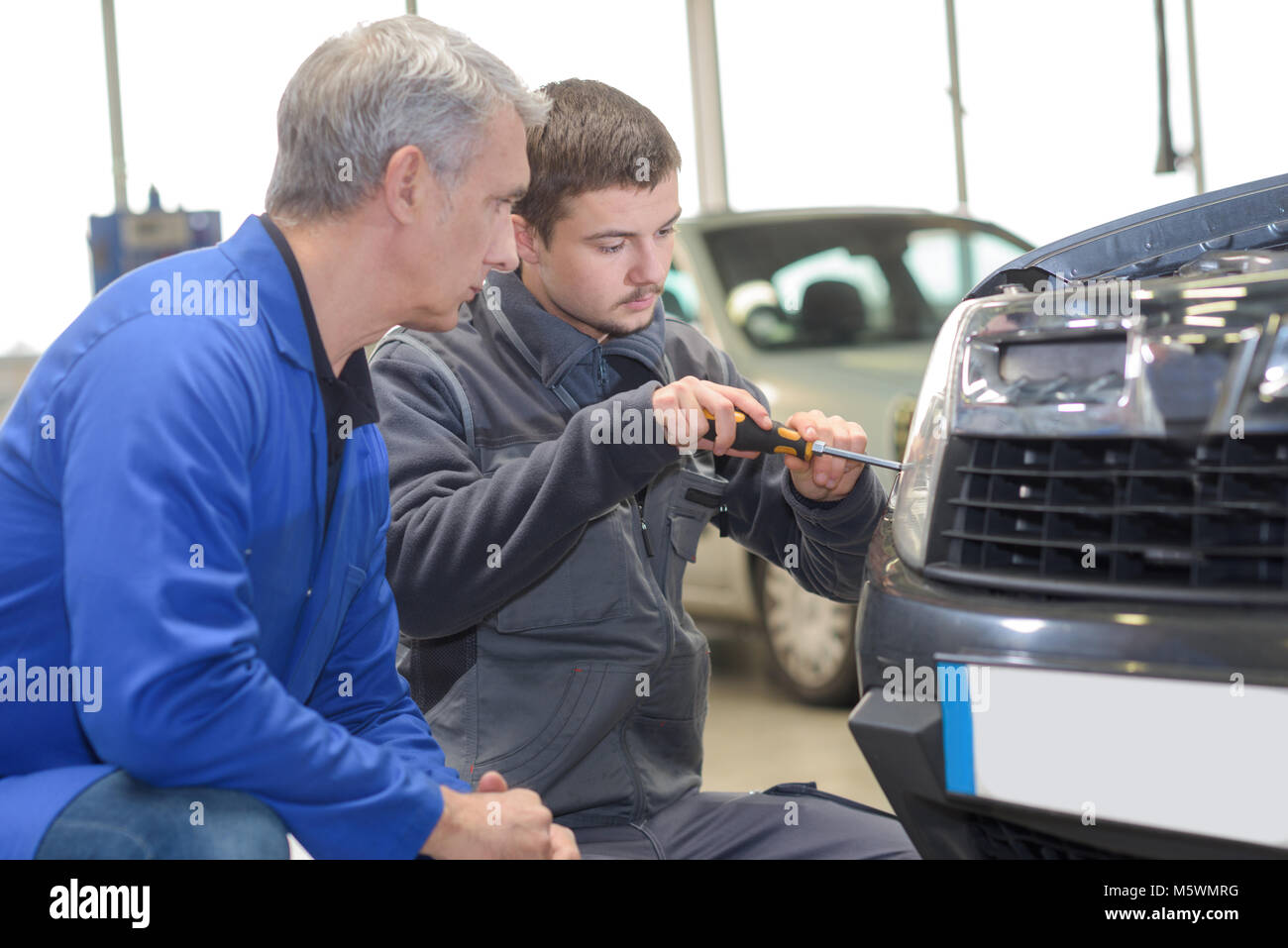 student and teacher mechanics changing car headlight in a workshop Stock Photo