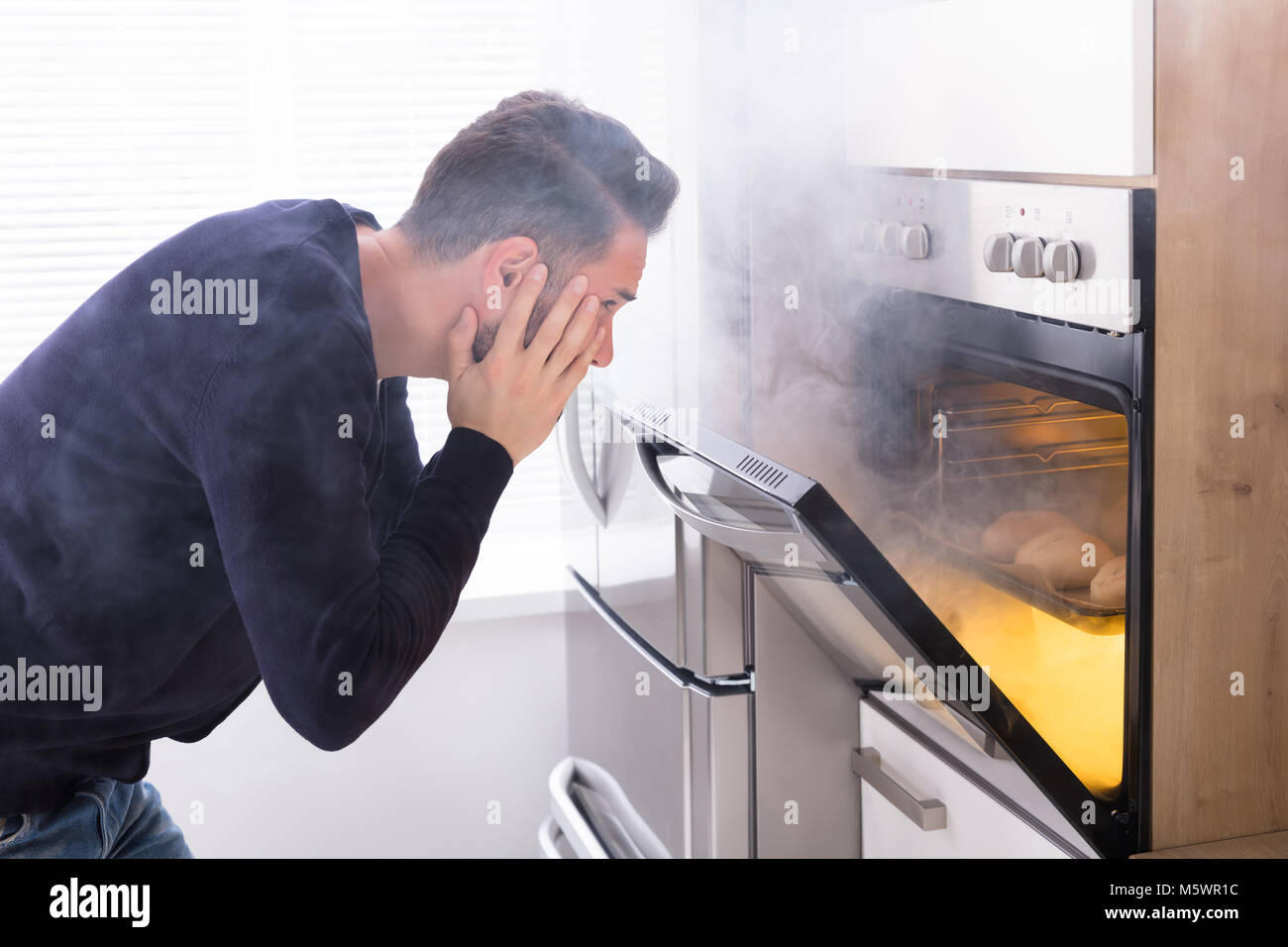 Shocked Man Looking At Burnt Cookies With Smoke Coming From Oven Stock