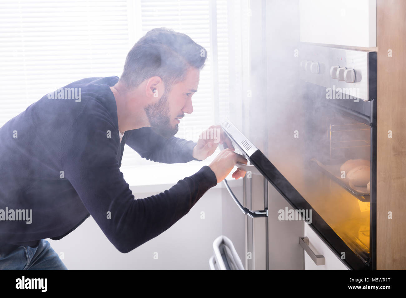 Shocked Man Looking At Burnt Cookies With Smoke Coming From Oven Stock