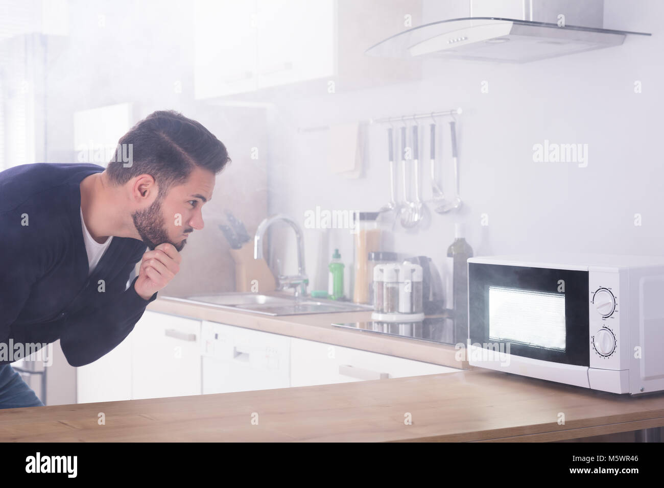 Young Man Spraying Fire Extinguisher On Microwave Oven In The Kitchen