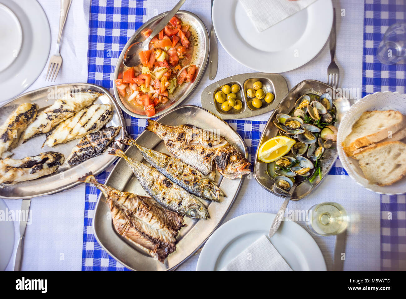 Fish feast: sea bass, golden, horse mackerel accompanied with tomato salad, clams, bread and white wine, Portugal Stock Photo