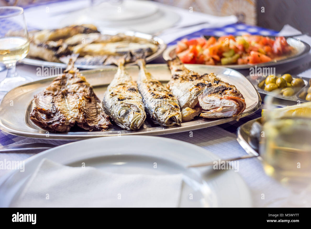 Fish feast: sea bass, golden, horse mackerel accompanied with tomato salad, green olives and white wine, Portugal Stock Photo