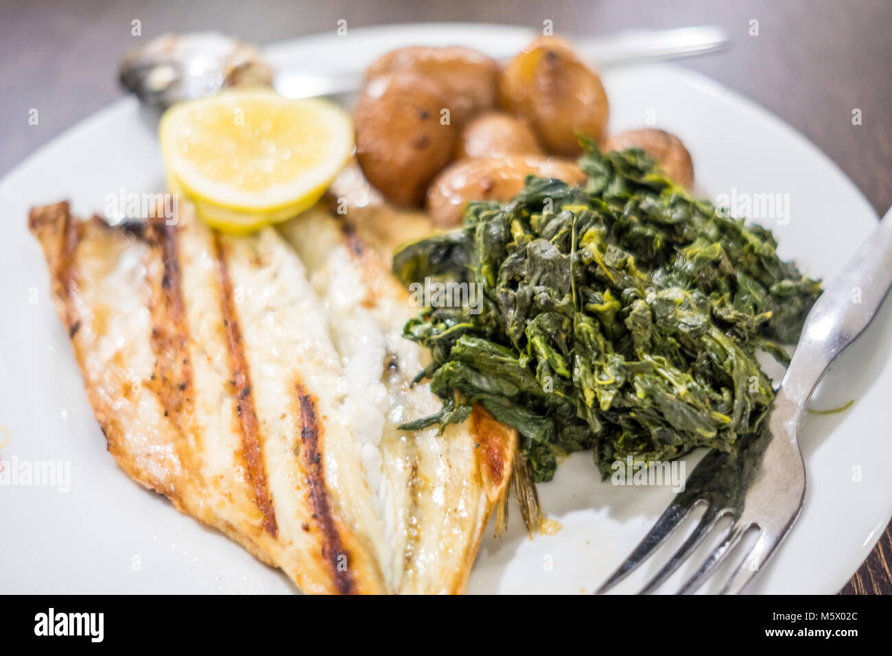Barbecued sea bass served with lemon, baked potatoes and spinach on