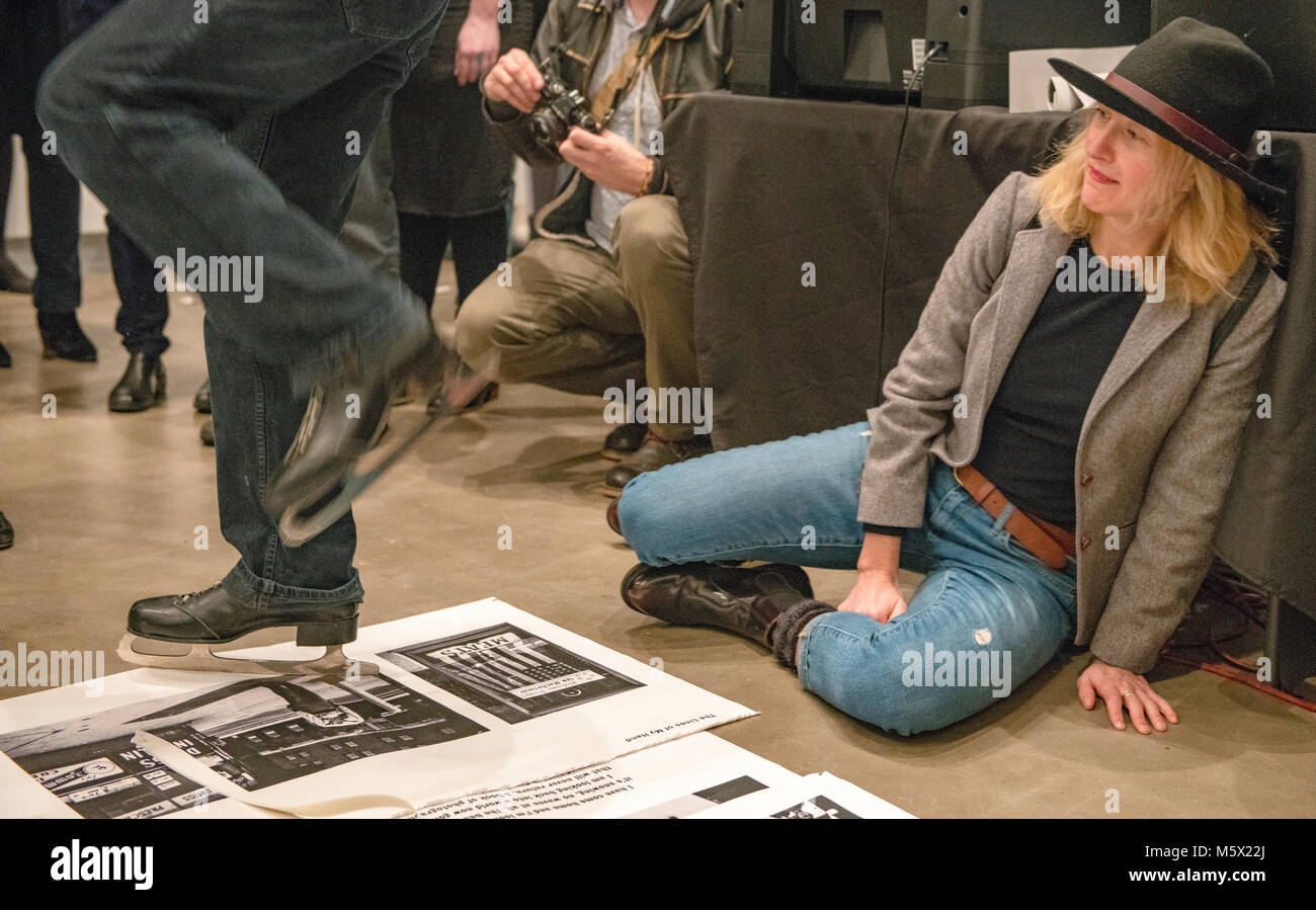 Portland, Oregon, USA. 26 FEB, 2018. The photographer Leah Nash avoids the blades of an ice skating performance artist as he shreds  photographer Robert Frank’s work at Blue Sky Gallery in Portland, Oregon, USA. The work was destroyed in a “Destruction Dance” performance defacing the photographs with ink and mutilation with scissors, knives and even ice skates  at the end of it’s run. The destruction was Frank's protest regarding today's greed in the global art market. Credit: Ken Hawkins/Alamy Live News Stock Photo