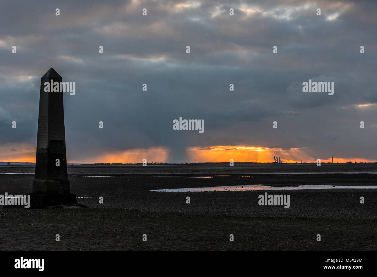 Snow arrived in the Southend Borough at dusk, as the sun set behind the Crowstone at Chalkwell, Essex, UK. Thames Estuary at low tide. PLA limit marker Stock Photo