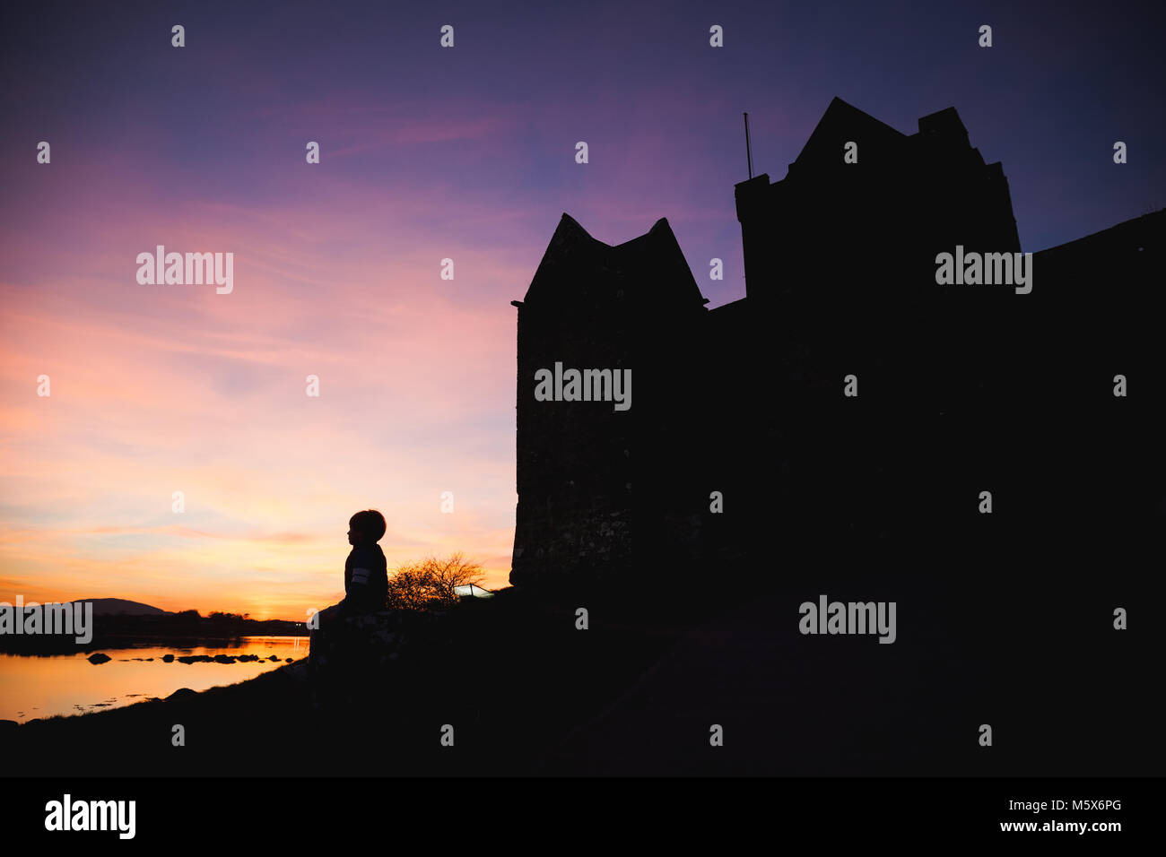 Boy looking at colorful sunset at the ocean bay with Castle siluette. Stock Photo