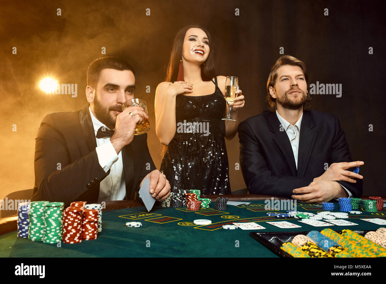 Group of young rich people is playing poker in the casino. Two men in  business suits and a young woman in a black dress. Smoke. Casino. Poker  Stock Photo - Alamy