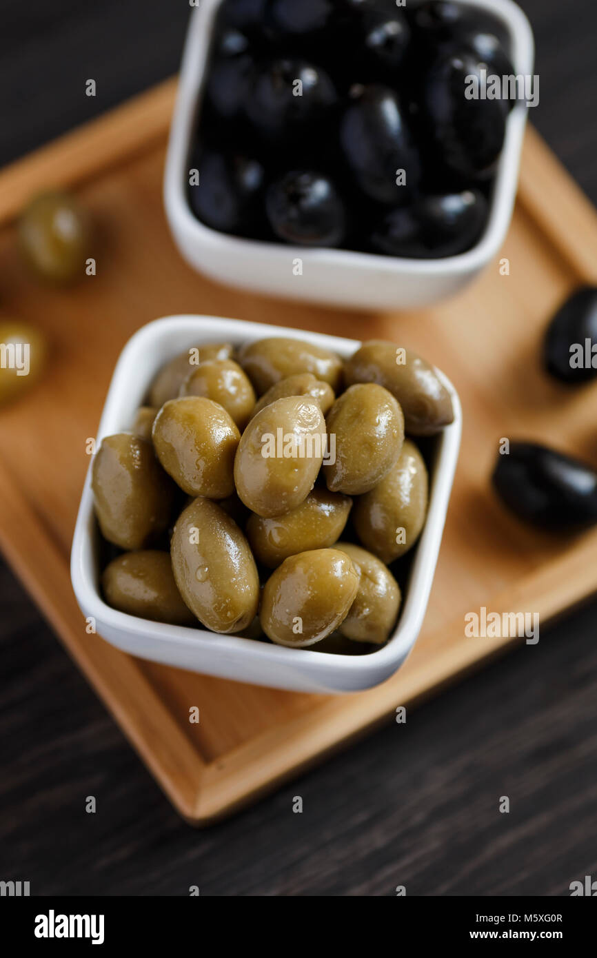 Black and green olives in a white bowl on a dark wooden table. Stock Photo