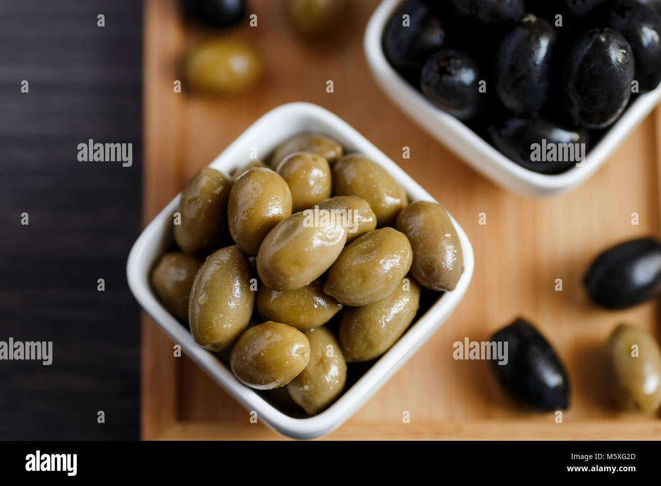 Black and green olives in a white bowl on a dark wooden table. Stock Photo