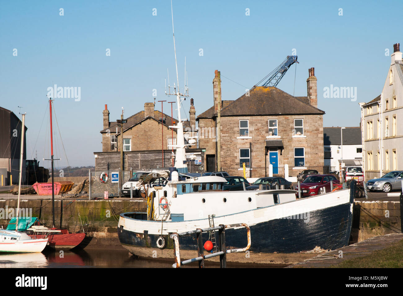 Boats in low water dock and house with a crane behind roof of house in industrial quayside area at Glasson Dock Lancashire Stock Photo