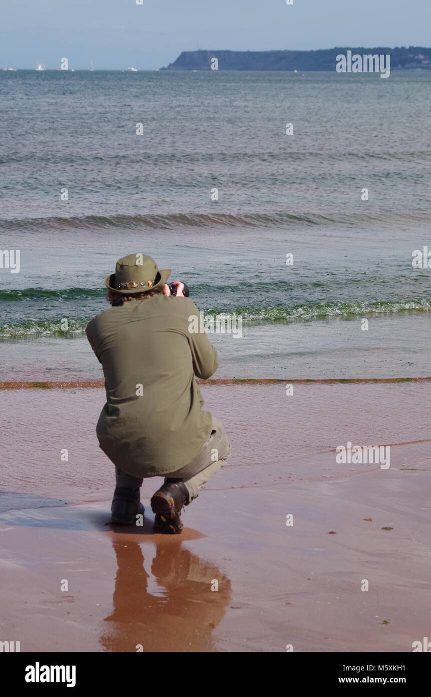 Young British Man Dressed In Green Photographing Small Waves On young-british-man-dressed-in-green-photographing-small-waves-on