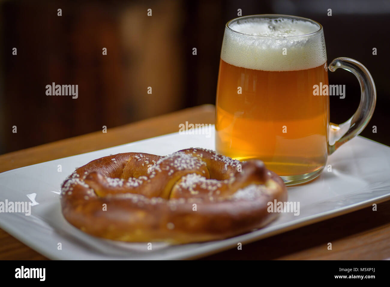 macro closeup of a large glass mug of beer and a warm soft pretzel on a plate Stock Photo