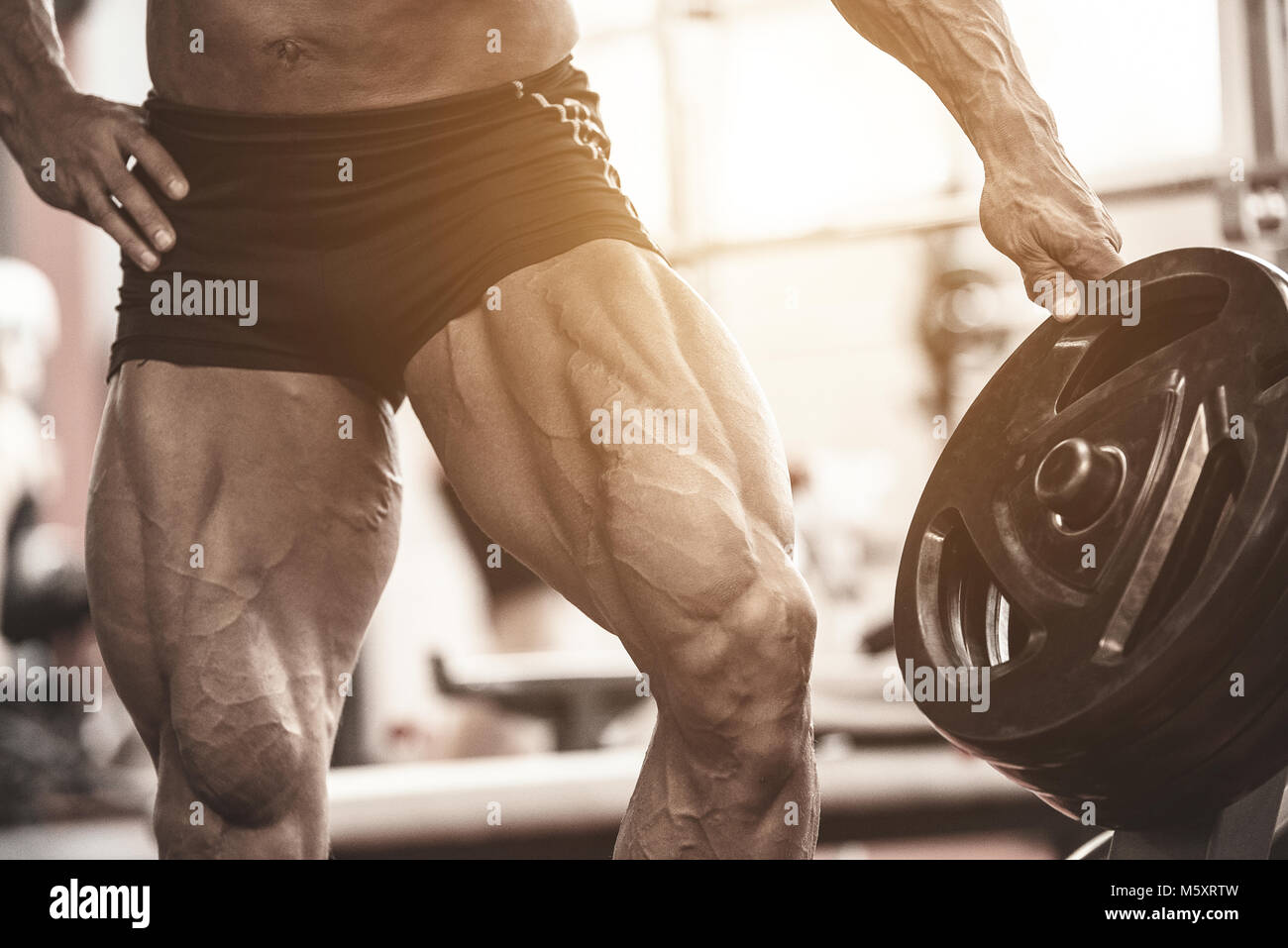 Close-up of bodybuilders muscular legs. Athlete man doing workout exercise in gym Stock Photo
