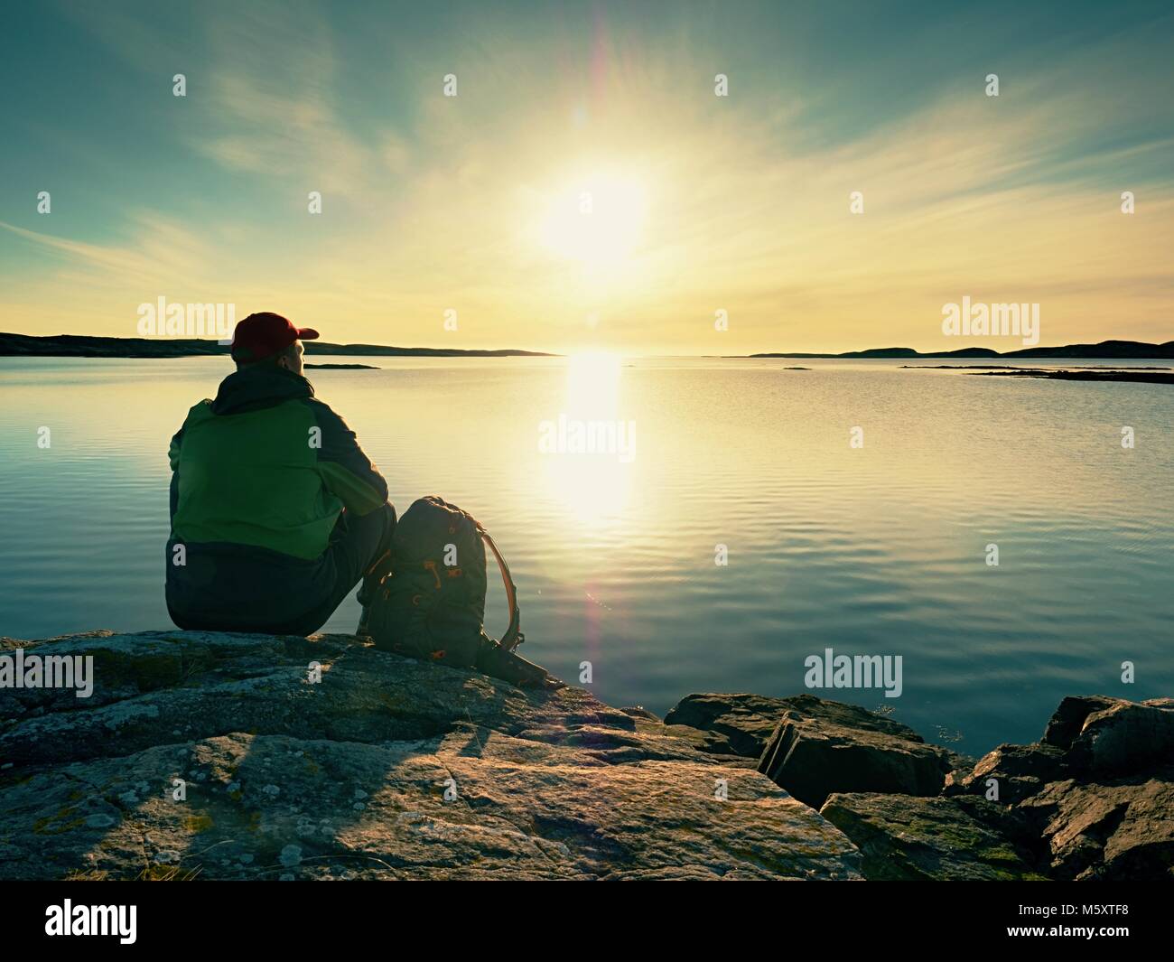 Young man sitting on a rock watching a gorgeous sunset on the sea ...