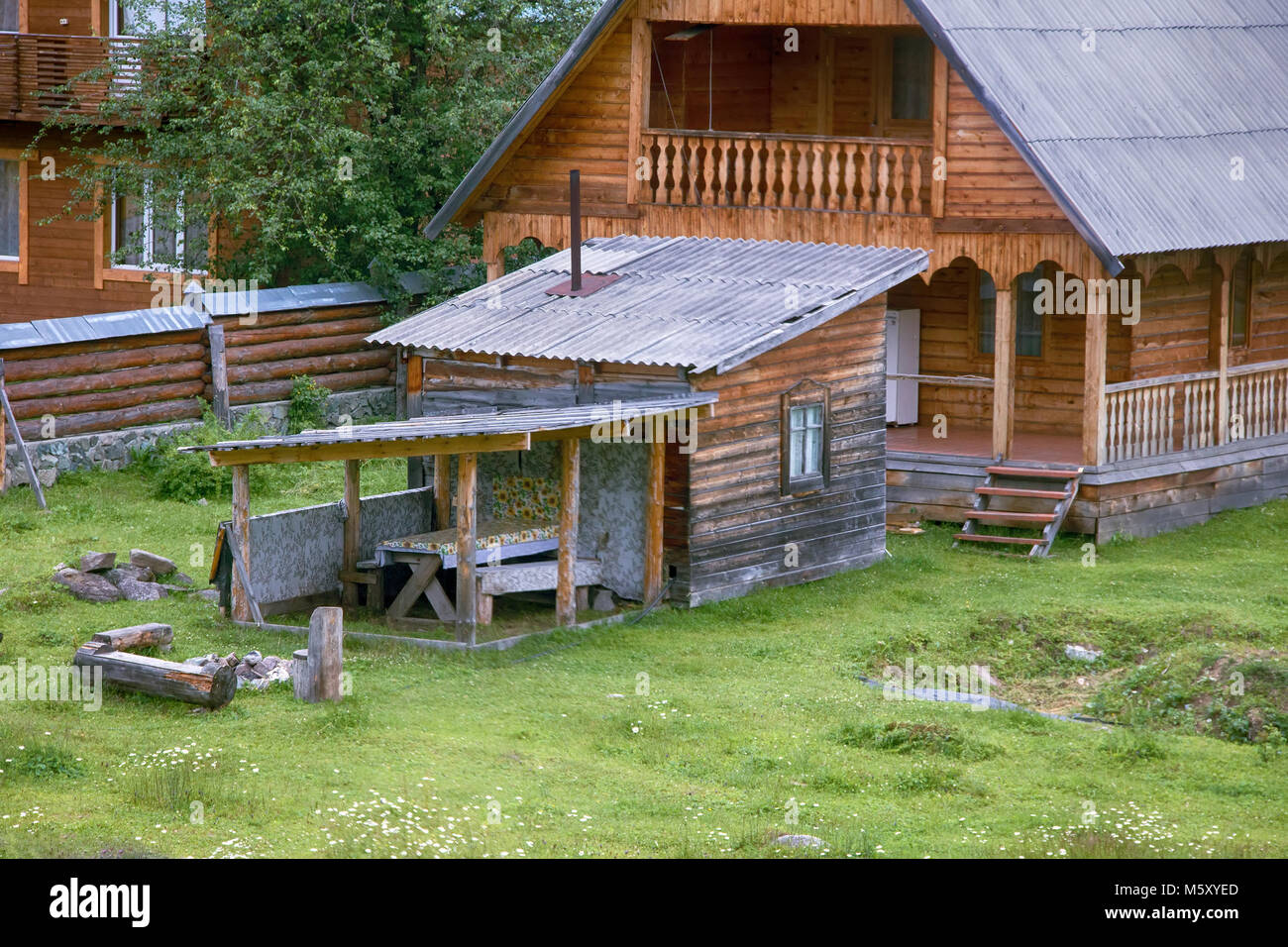 House in Russian village single family. House with carved architraves and veranda. small summer kitchen for cooking in warm season. Altai. Stock Photo