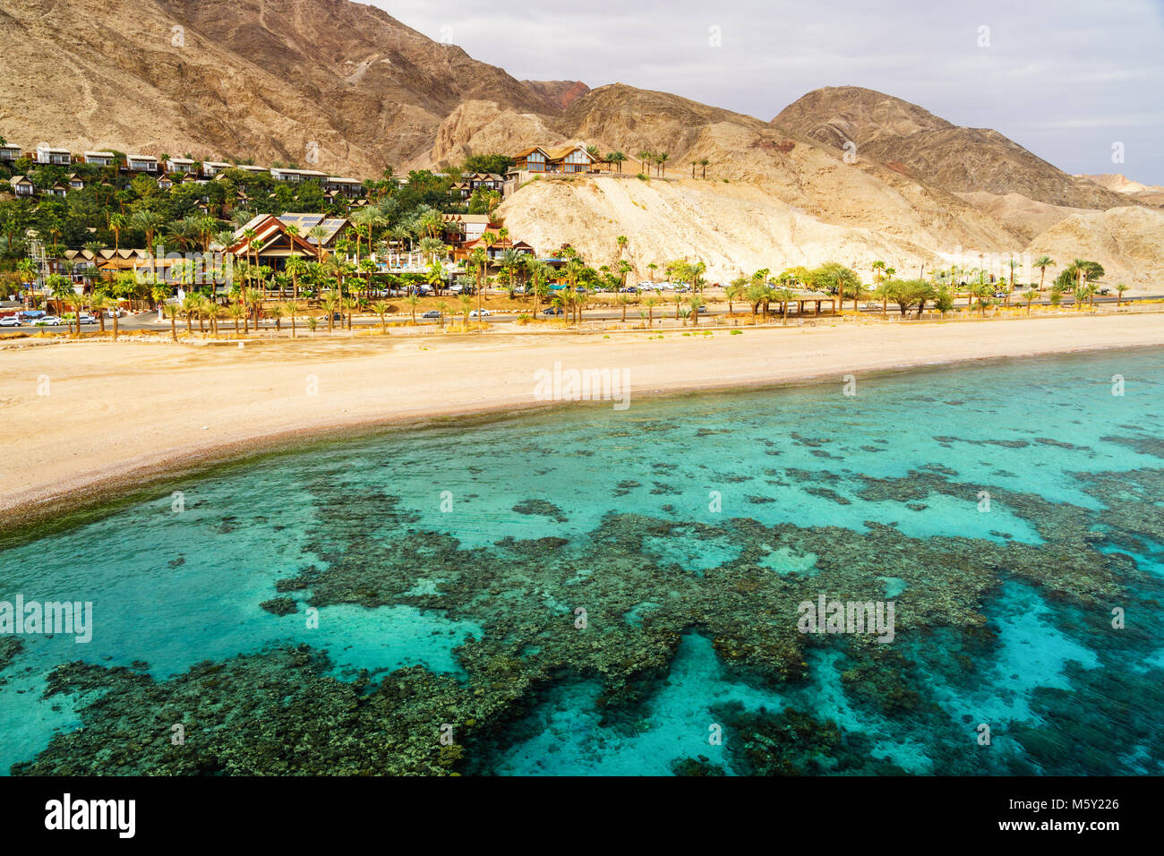 Coral reef of Aqaba Bay in Red Sea, empty beach and desert near Eilat, Israel. Contrast between turqoise coral sea and dry desert. Travel theme. Stock Photo