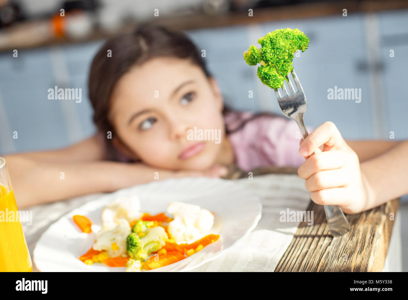 Sad girl looking at the vegetable on her fork Stock Photo