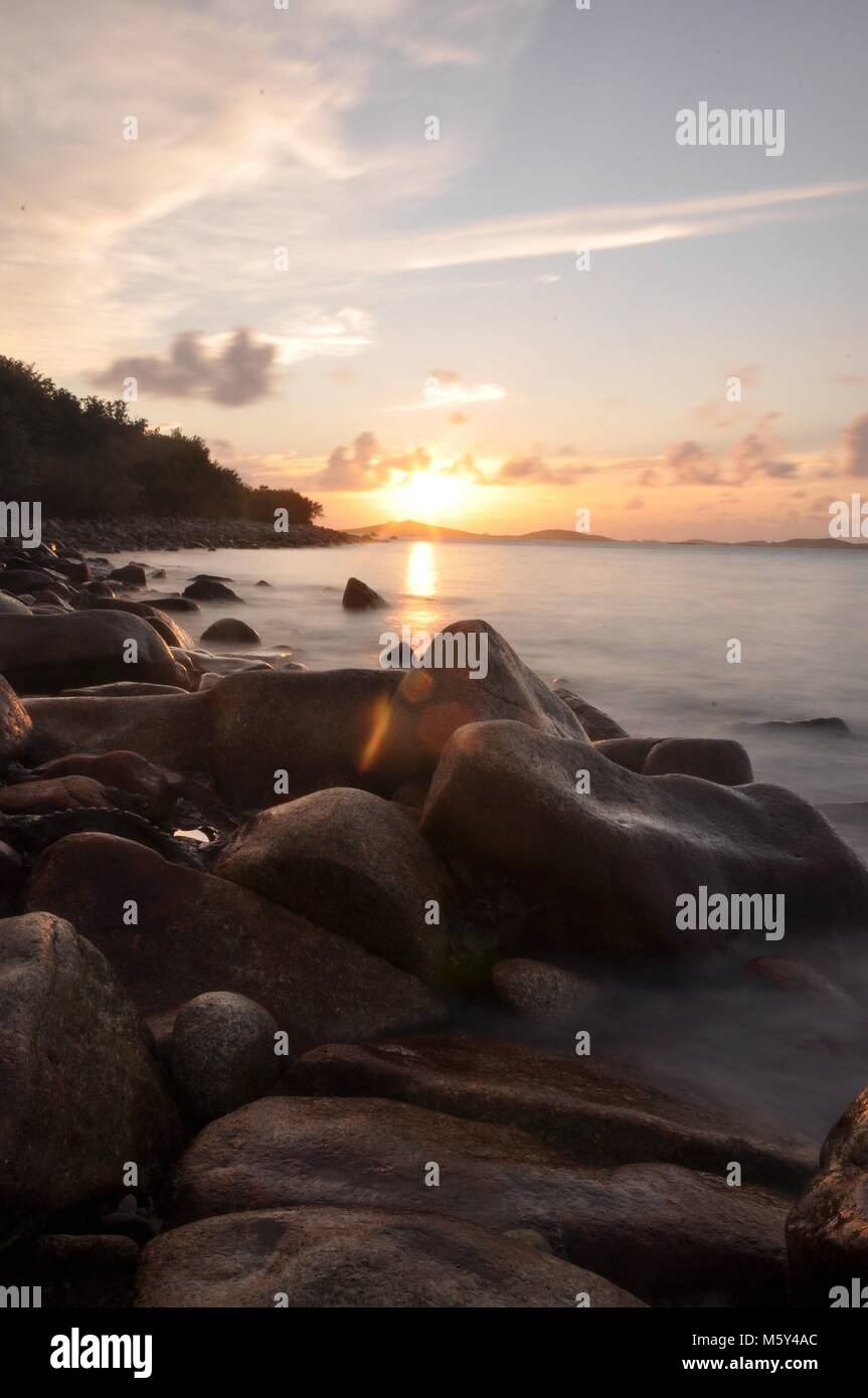 Sunset seascape across rocky coastline with long exposure and soft water. Isles of Scilly, views across the sea to Samson island at sunset. Stock Photo