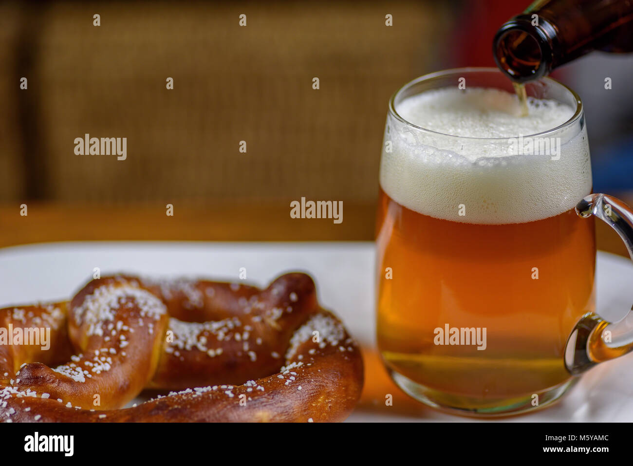 pouring beer into a large glass mug on plate with warm soft pretzel
