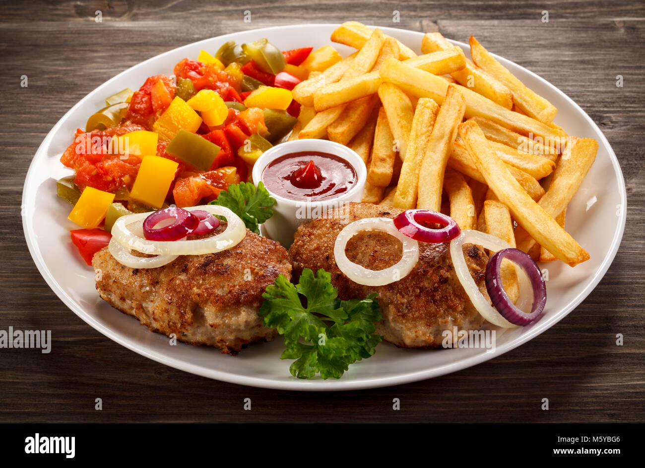 Fried chops, French fries and vegetable salad on wooden table Stock