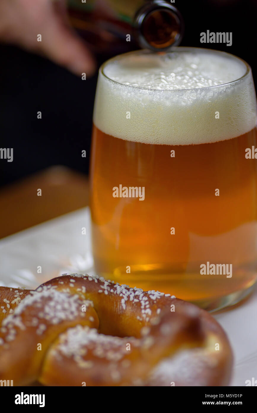 pouring beer into a large glass mug on plate with warm soft pretzel