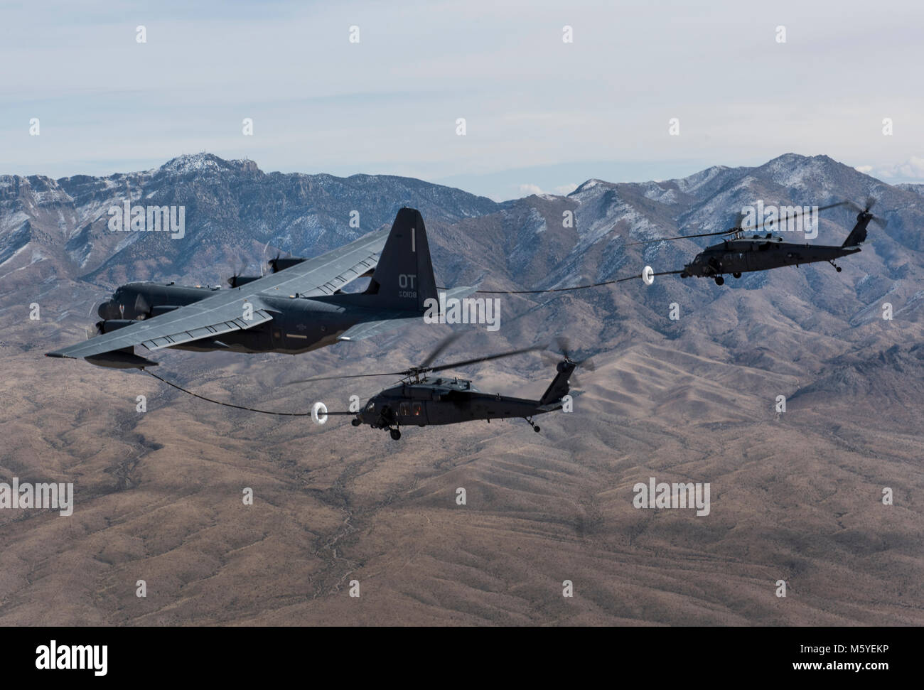 A pair of HH-60 Pave Hawk helicopters receive fuel from a HC-130J Combat King II cargo aircraft during a training mission over the Nevada Test and Training Range Feb. 22, 2018. The HC-130J is designed to conduct personnel recovery missions, provide a command and control platform, in-flight refuel helicopters, and carry supplemental fuel for extending range or air refueling. (U.S. Air Force photo by Senior Airman Kevin Tanenbaum) Stock Photo