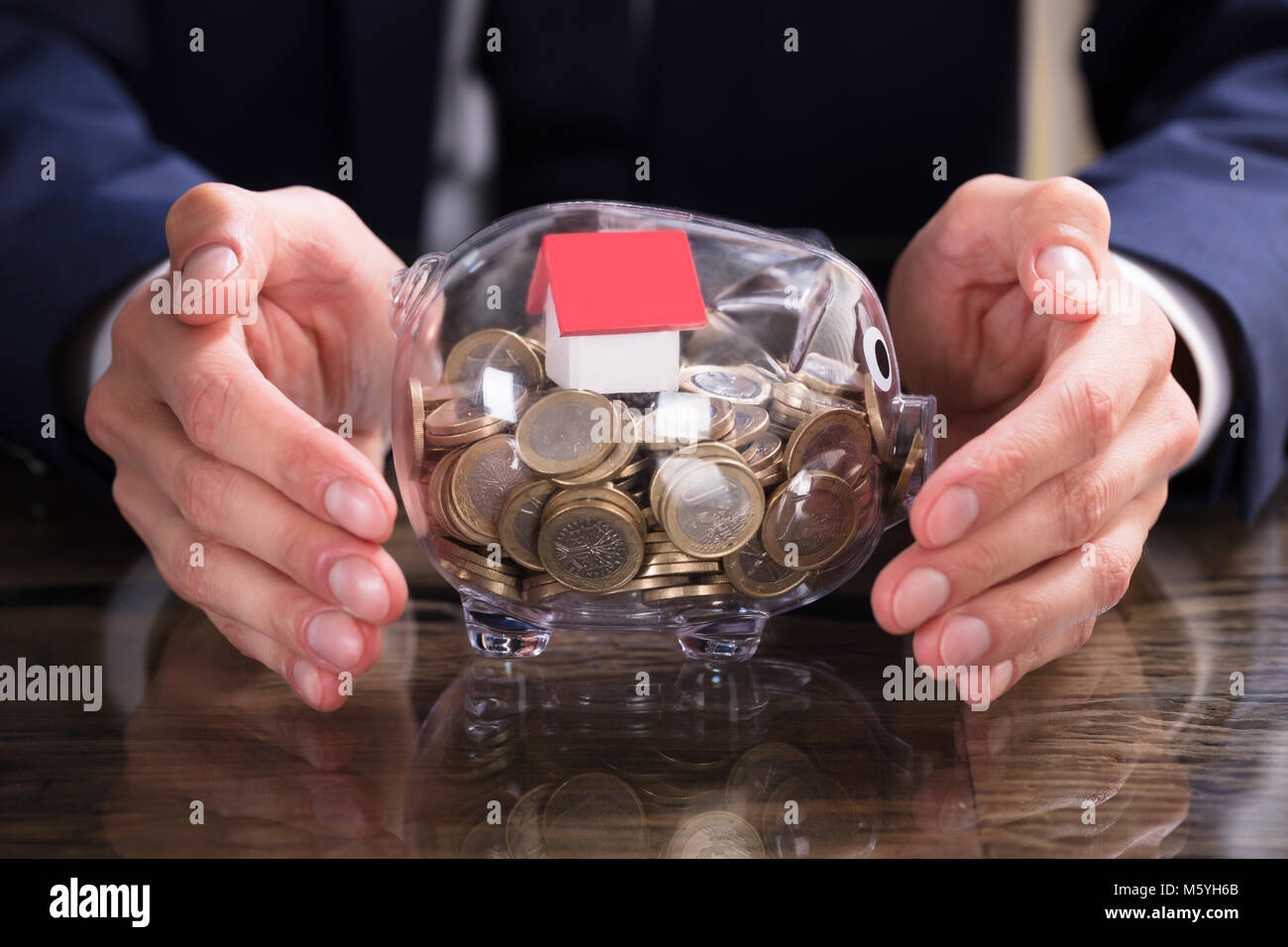 Close-up Of A Businessperson's Hand Protecting House Model And Coins Inside Piggybank Stock Photo