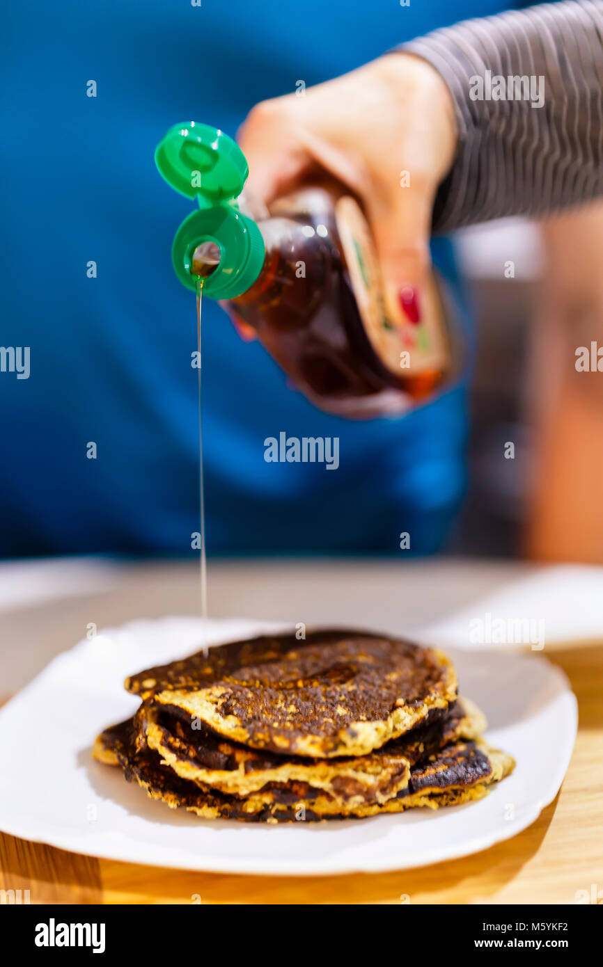 cropped shot of person pouring maple syrup onto stack of pancakes Stock