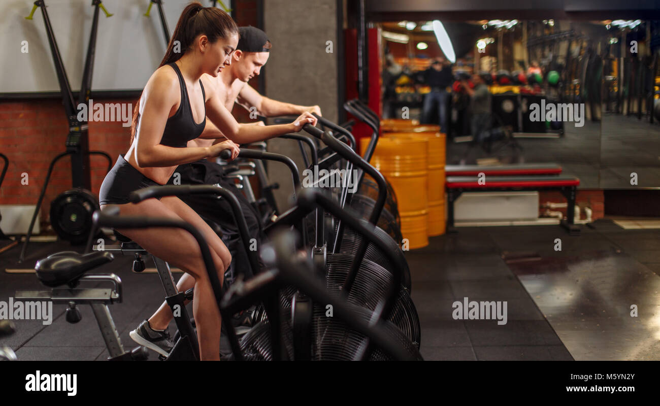 woman and man biking in gym, exercising legs doing cardio workout cycling bikes Stock Photo