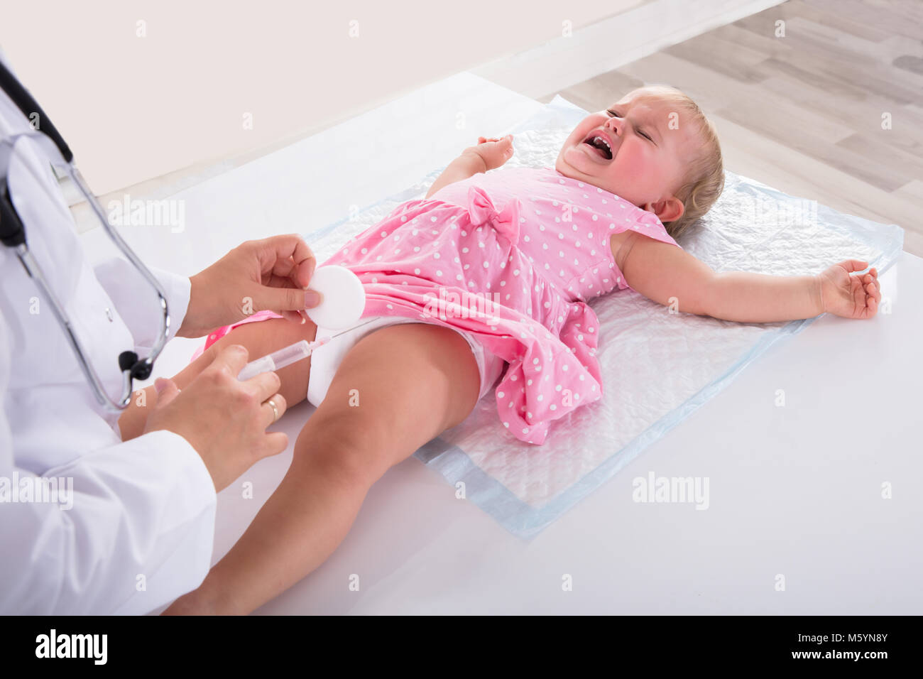 Doctor Giving Vaccine Injection To Crying Baby Girl In Clinic Stock Photo