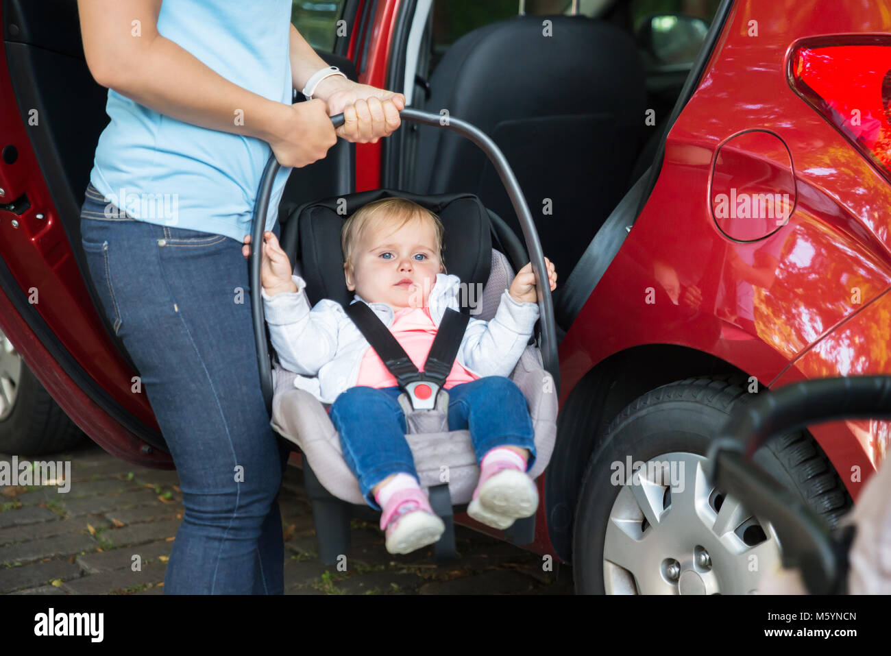 Mother Carrying Baby On Seat Outside Red Car Stock Photo