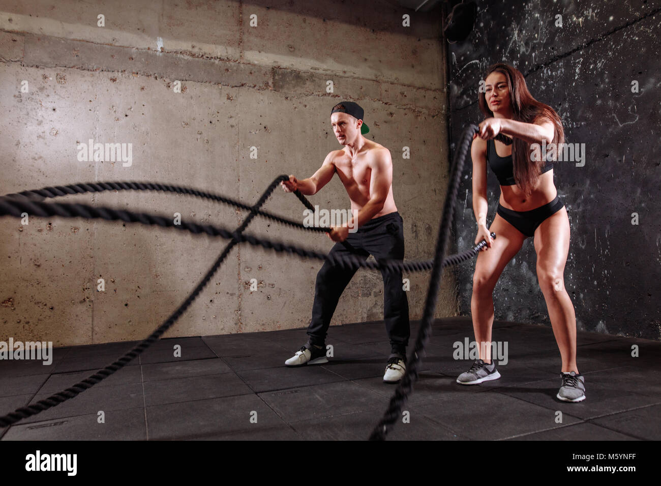 Woman and man couple training together doing battling rope workout ...
