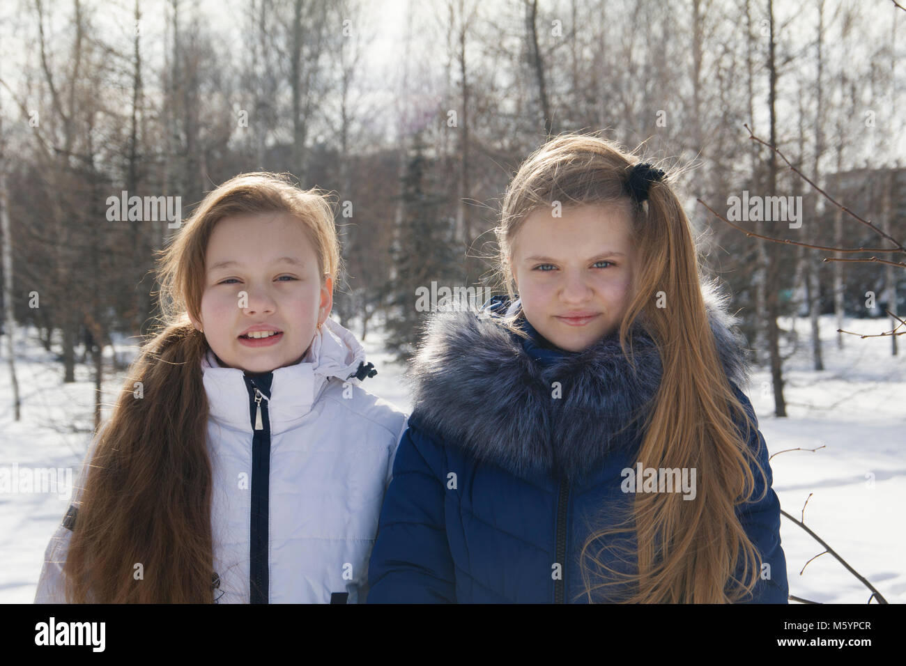 Portrait of two teen girls in warm clothes between the trees in winter Stock Photo