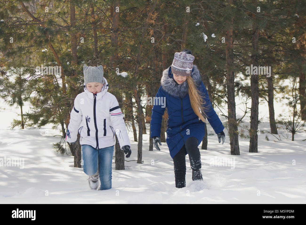 Two teenage girls in warm clothes walking through the snow between the trees in the winter Stock Photo