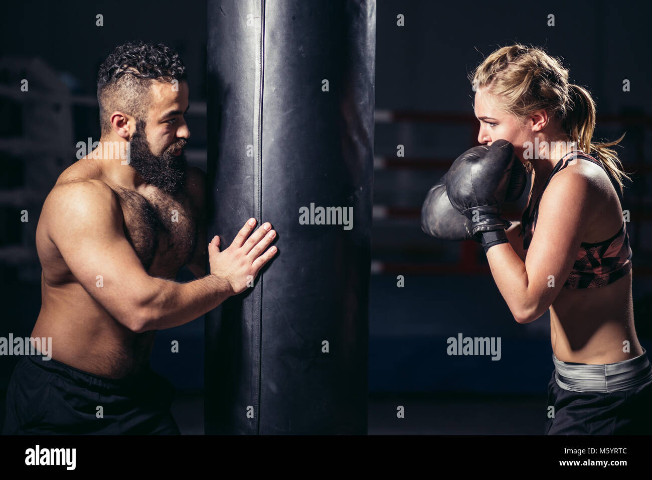 woman working out with boxing gloves and punching bag with her trainer. Stock Photo