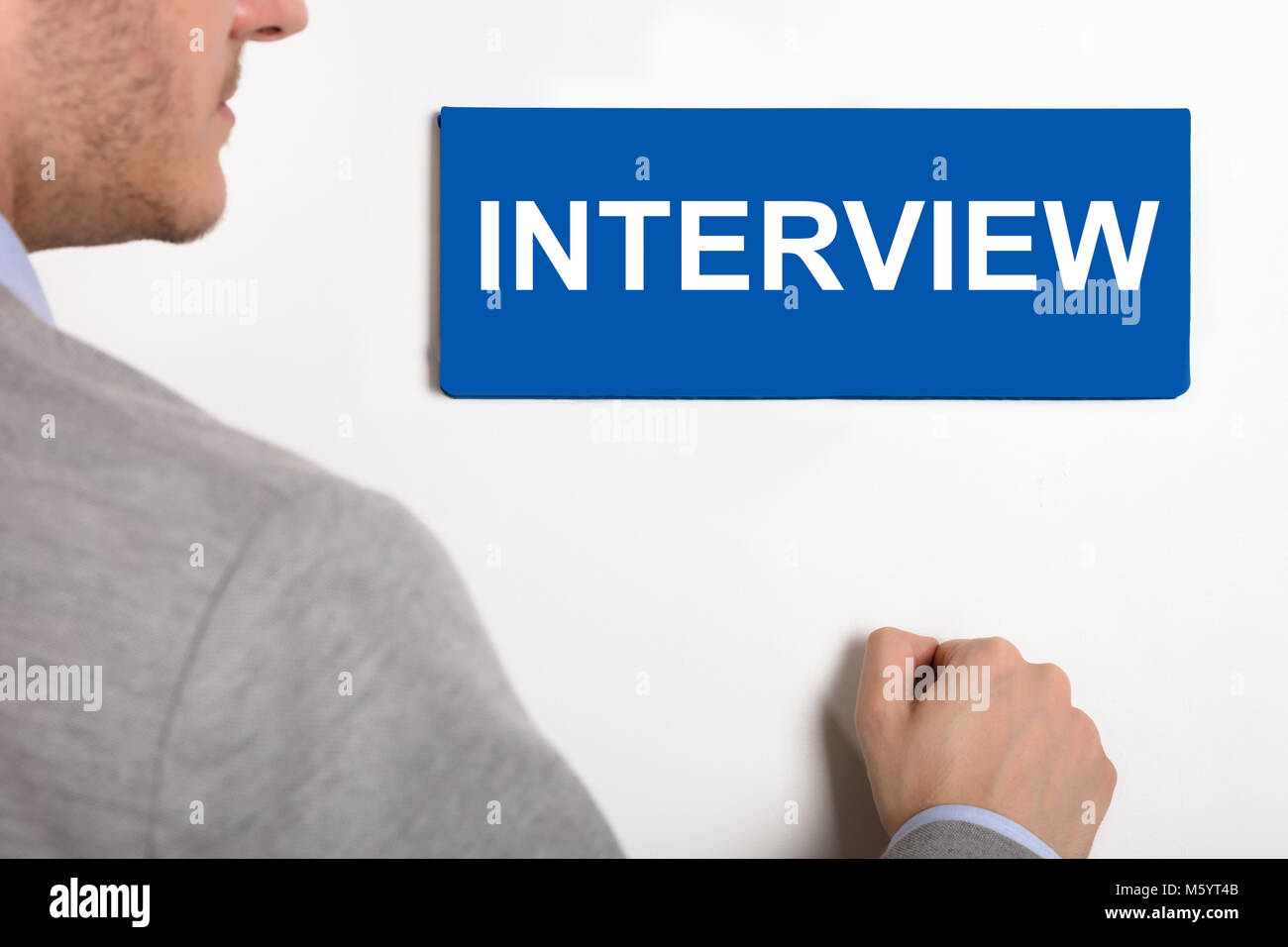Close-up Of A Young Businessman Knocking White Door With Interview Nameplate Stock Photo