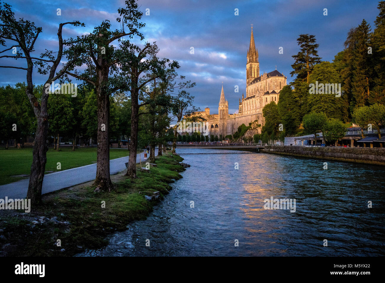 Lourdes (south-western France). The Basilica of Our Lady of the Rosary, built above the Grotto of Massabielle, viewed at sunset from the banks of the  Stock Photo