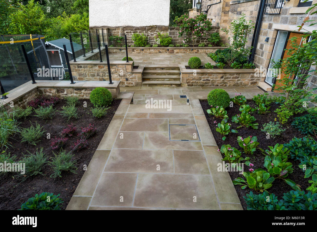 Small corner of beautiful, landscaped, private garden with contemporary design, paved path & steps, border shrubs & plants - Yorkshire, England, UK. Stock Photo