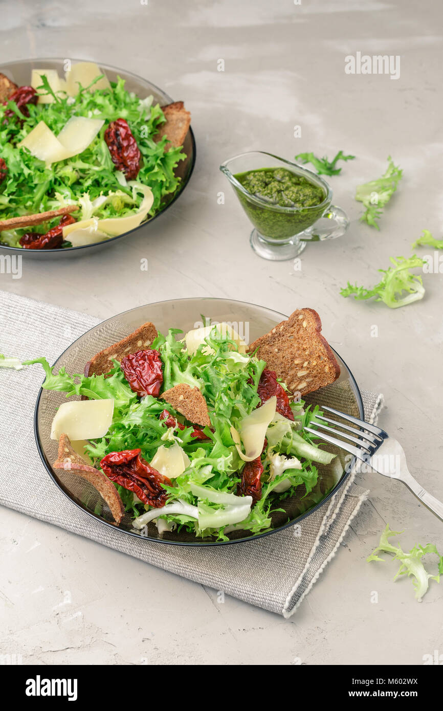 Salad with frisee lettuce, sun dried tomatoes, cheese, bread chips and pesto dressing Stock Photo